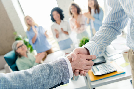 Business handshake in office with coworkers applauding for teamwork and success