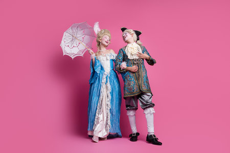 A couple dressed in elaborate baroque costumes, posing gracefully against a vibrant pink backgroundの写真素材