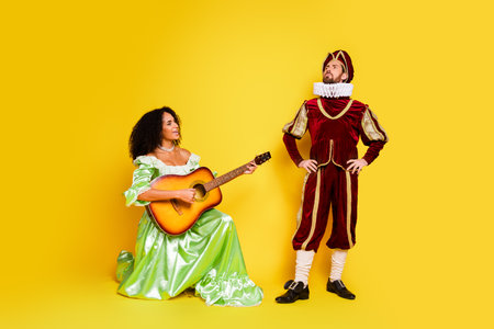 Elegant couple in historical costumes posing against a vibrant yellow backdrop portraying medieval nobility and musical creativityの写真素材