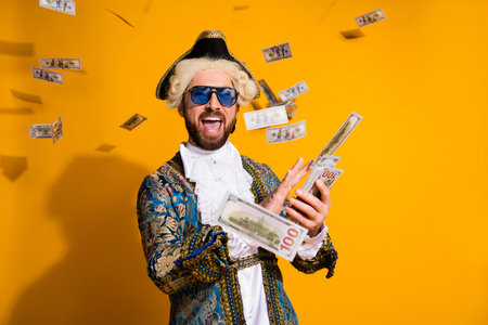 Portrait of a nobleman in vintage costume enjoying celebration with banknotes on bright yellow backgroundの写真素材