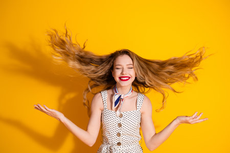 Smiling young woman with flowing hair in a polka dot dress on a vibrant yellow background, exuding joy and confident charmの写真素材