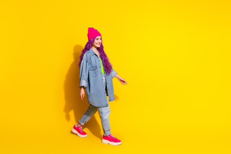 Portrait of a stylish young woman wearing vibrant clothing on a yellow background, showcasing a cheerful and trendy attitudeの写真素材