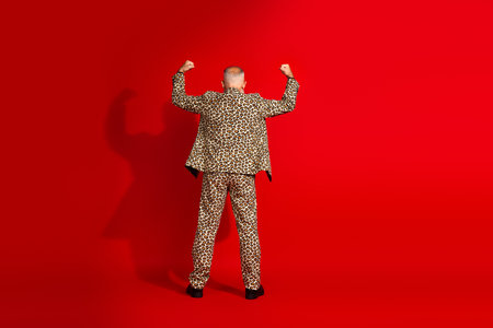 Stylish man in leopard print suit posing confidently with a red background emphasizing elegance and charismaの写真素材