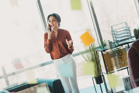 Confident young businesswoman conversing on a phone in an office setting surrounded by notesの写真素材
