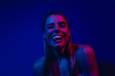 Young woman posing under neon blue and pink lights, showcasing beauty and vibrant energy with a stylish disco inspired aestheticの写真素材