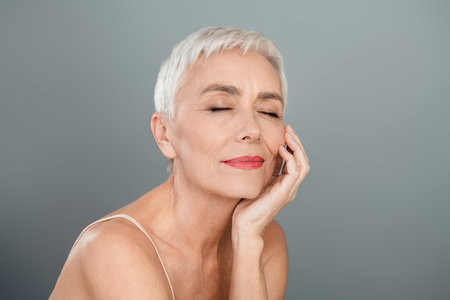 Tender mature woman with short blonde hair posing against a neutral background showcasing natural beauty and skin careの写真素材