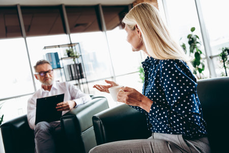 Mature businessman and businesswoman discussing collaboration in a meeting while seated in a bright and modern office spaceの写真素材