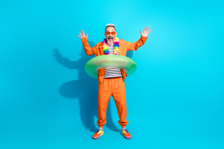 Charismatic Mature Man in Stylish Orange Suit with Inflatable Ring Celebrating on Blue Background in a Cheerful Poseの写真素材
