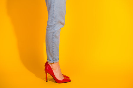 Stylish young woman in red heels standing against a vibrant yellow backdrop, showcasing trendy fashion and casual styleの写真素材