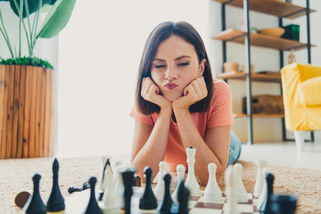 Charming girl in striped t-shirt playing chess, relaxing in stylish living room during a sunny dayの写真素材