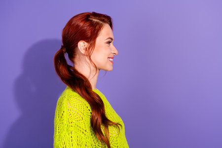 Side profile of a young red-haired woman wearing green knit sweater against purple background...
