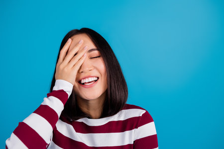 Joyful woman with hand covering her face in front of blue backgroundの写真素材