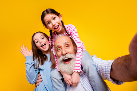 Happy grandfather and granddaughters enjoying a joyful moment with a bright yellow backgroundの写真素材