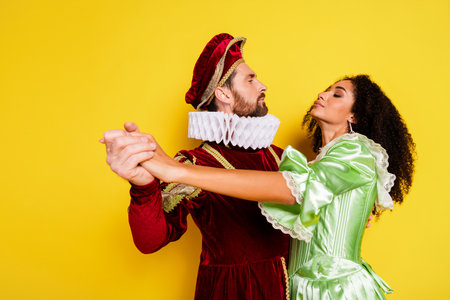 Elegant couple in historical costumes dancing against vibrant yellow background showcasing retro royal fashionの写真素材