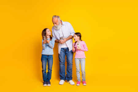 Elderly man with his two granddaughters holding smartphones against a vibrant yellow backgroundの写真素材
