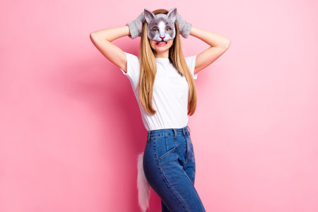 Portrait of a stylish young woman in a playful cat-themed costume posing against a pink backgroundの写真素材