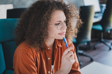 Young professional woman in a casual workplace environment contemplating ideas while working indoors with natural light.の写真素材