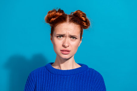Young Stylish Woman in Blue Sweater Against Bright Background Expressing Concernの写真素材
