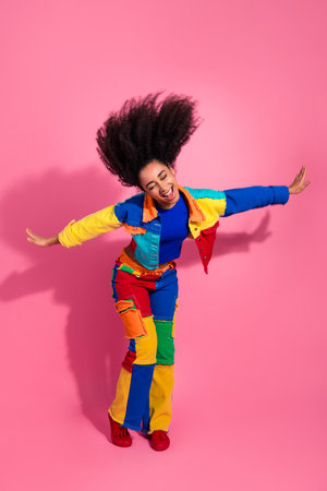 Vibrant young woman wearing colorful denim ensemble posing joyfully against a vivid pink backgroundの写真素材