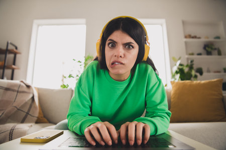 Young woman in a casual green sweatshirt expressing confusion while sitting in a cozy modern living...