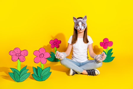 Young girl with cat mask sits crosslegged with yellow background and handdrawn flowers.の写真素材