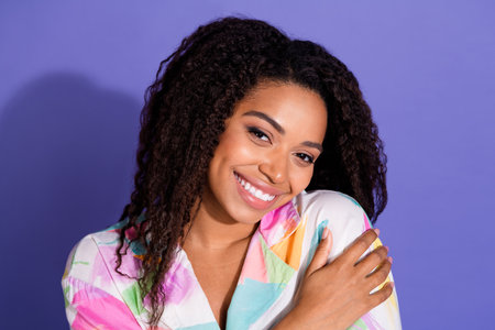 Charming young woman with a vibrant smile posing against a purple background, showcasing stylish...