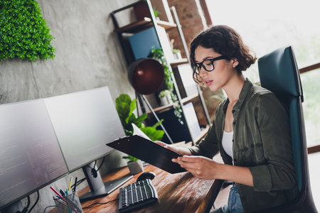 Young professional female software programmer reviewing project documents while working in a modern...