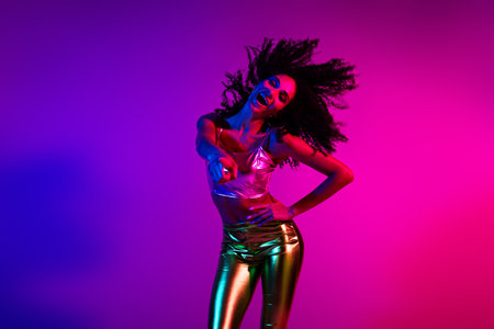 Energetic Young Woman in Glamorous Outfit Dancing in Neon Party Lightingの写真素材