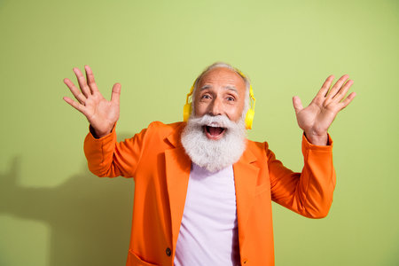 Portrait of funky eccentric grandfather raise arms open mouth headphones music wear orange suit isolated on green color backgroundの写真素材