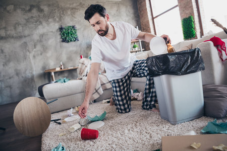 Photo of funky funny sad guy wear sleepwear mess dirty home after bachelor party clean house indoors apartment roomの写真素材