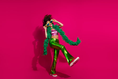 Trendy young woman dancing joyfully in glossy attire against vivid magenta backgroundの写真素材