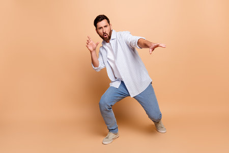 Confident young man striking an expressive pose on a beige background wearing casual stylish attireの写真素材