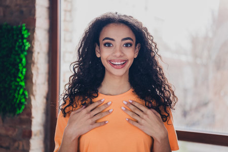 Young afro american woman indoors smiling brightly in orange t-shirt, enjoying a moment of joyful expression.の写真素材