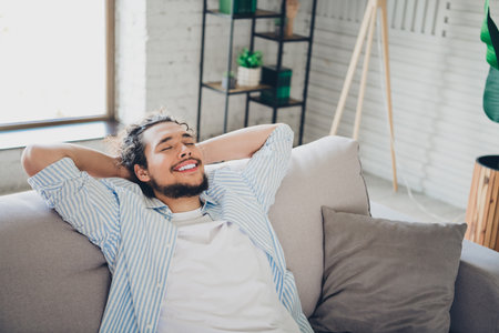 Joyful young man relaxing on comfortable couch in modern home interior