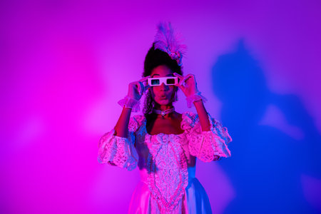 Elegant woman in vintage dress posing with fun 3D glasses against pink and purple neon lights...
