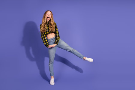 Excited young woman in trendy outfit posing against purple background with a joyful expressionの写真素材