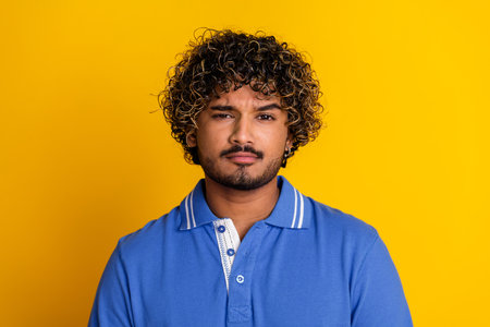 Stylish young man wearing a blue polo shirt standing in front of a vibrant yellow backgroundの写真素材