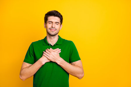 Portrait of his he nice attractive peaceful kind grateful guy wearing lilac shirt touching heart closed eyes isolated over bright vivid shine vibrant yellow color backgroundの写真素材