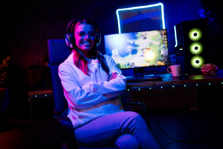 Photo of blonde girl sit armchair crossed hands confident play gamer computer game late night blue purple indoors house late neon lightの写真素材