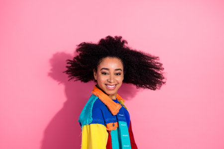Young woman with natural hair and colorful jacket smiling against a pink background