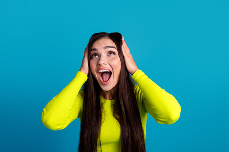 Energetic young woman in a vibrant yellow top expressing excitement against a bright blue...