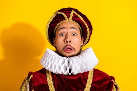 Portrait of man dressed as medieval nobleman with funny expression on a yellow background for a...