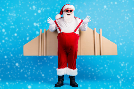 Full size photo of fat white grey hair bearded santa claus have card board wings pull suspenders x-mas christmas aviator travel wear suspenders overall isolated blue color backgroundの写真素材