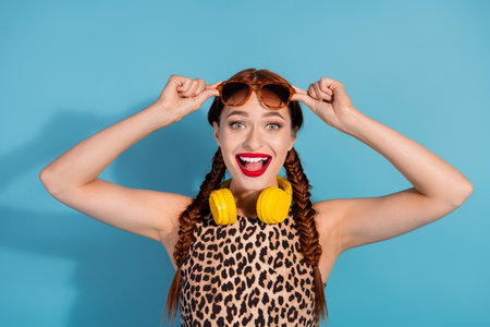 Cheerful young woman with braided hair and vibrant makeup posing playfully, wearing yellow...