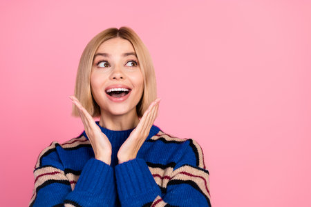 Charming Young Woman in Striped Sweater Expressing Excitement on Pink Backgroundの写真素材