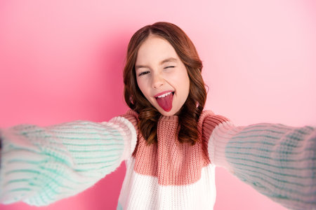 Young sweet girl posing playfully with a bright smile against a vibrant pink background, wearing a colorful sweaterの写真素材