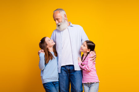 Elderly man spending joyful moments with two young girls against vibrant yellow background