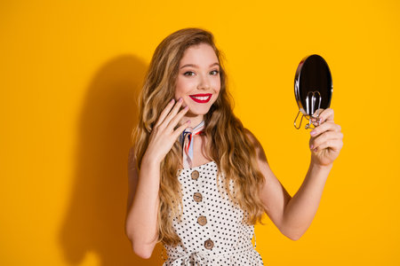 Portrait of a Smiling Young Woman Holding a Mirror Against Yellow Backgroundの写真素材
