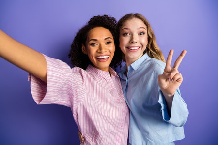 Young female friends taking a cheerful selfie against a purple background while celebrating together...