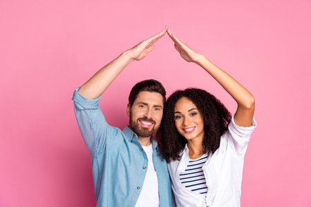 Young couple making a house gesture on pink background symbolizing love and togethernessの写真素材